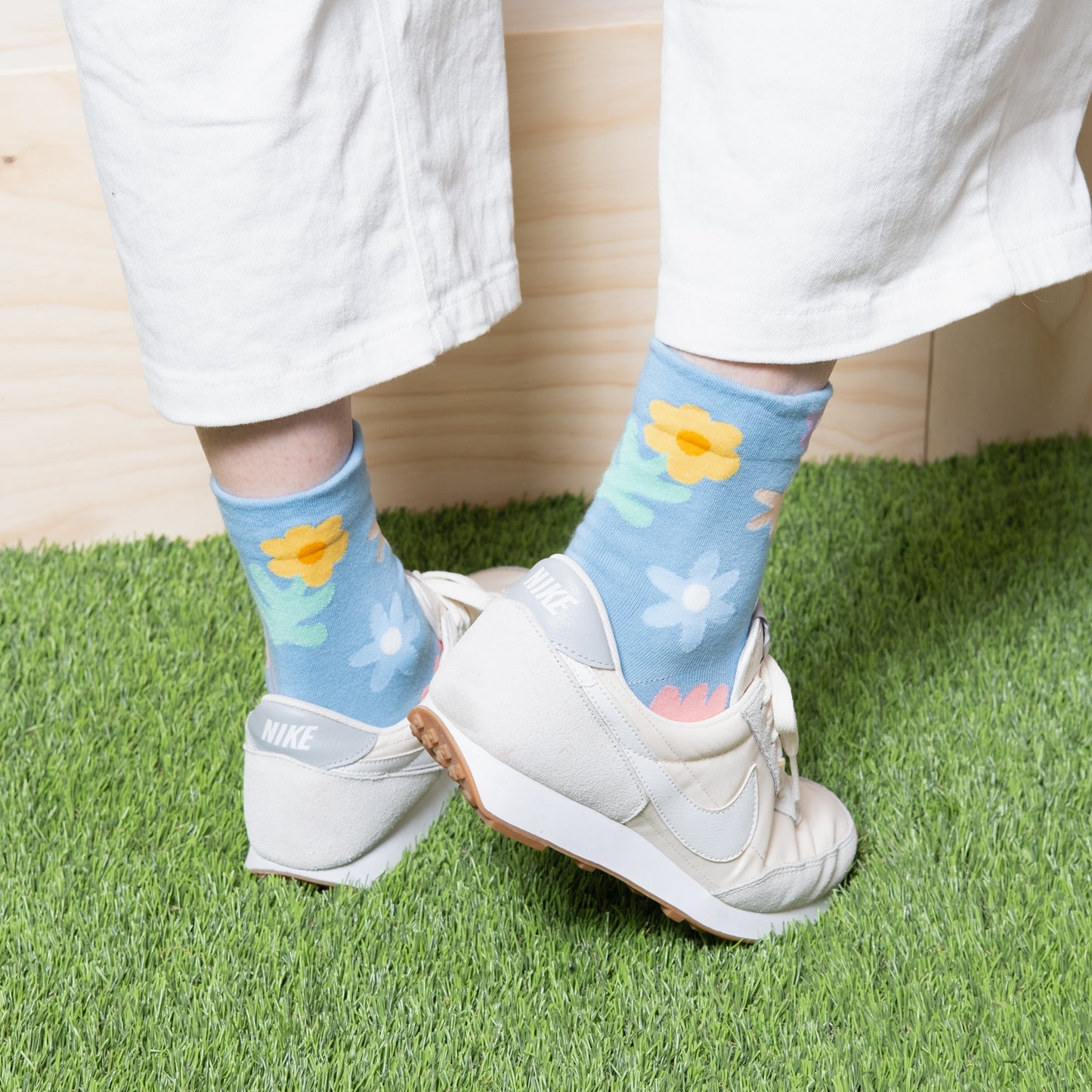 back view of Woman wearing luxurious sky blue ankle socks with fun cute multi color floral patterns with white pants and white nike sneakers