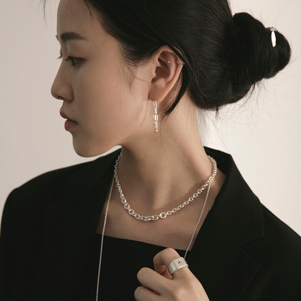 An Asian woman wearing black clothes and handmade silver connect chain necklace and a thin silver necklace and a ring with a cross and connect earrings