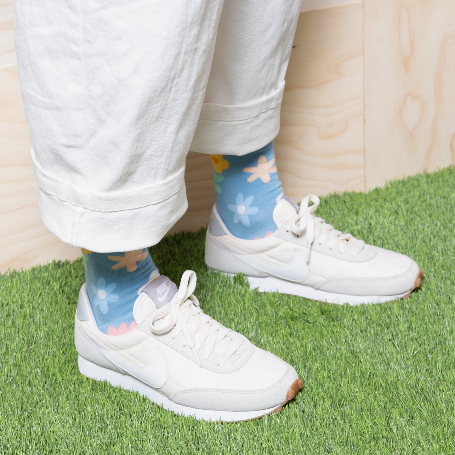 Woman wearing luxurious sky blue ankle socks with fun cute multi color floral patterns with white pants and white nike sneakers