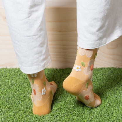 back view of woman wearing soft yellow textured floral socks with white pants 