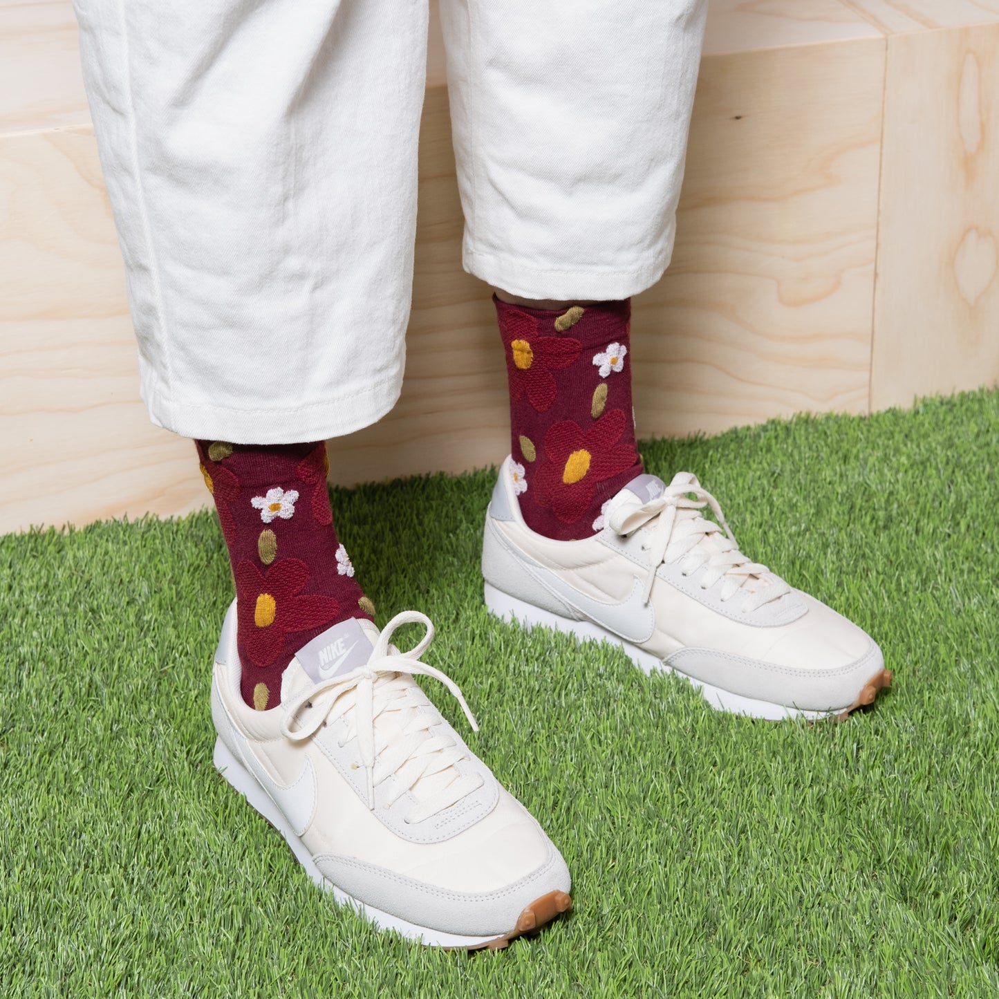 Woman wearing dk red textured floral socks with white patns and white sneakers